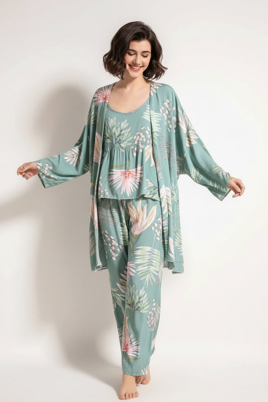 A woman wearing a green floral print cotton pyjama set consisting of a long robe, pants, and a vest.