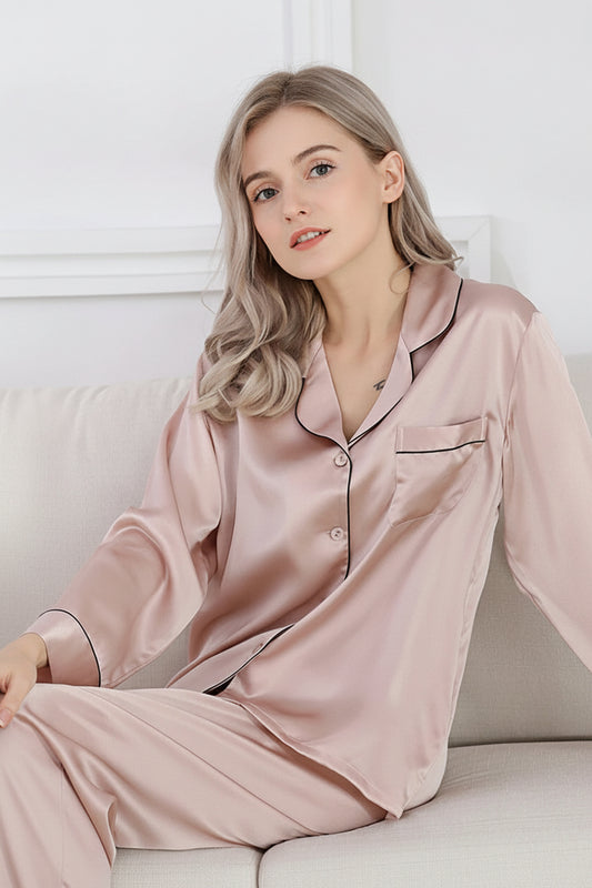 A woman sitting on a couch wearing a pink 100% silk pyjama set with long sleeves and pants.