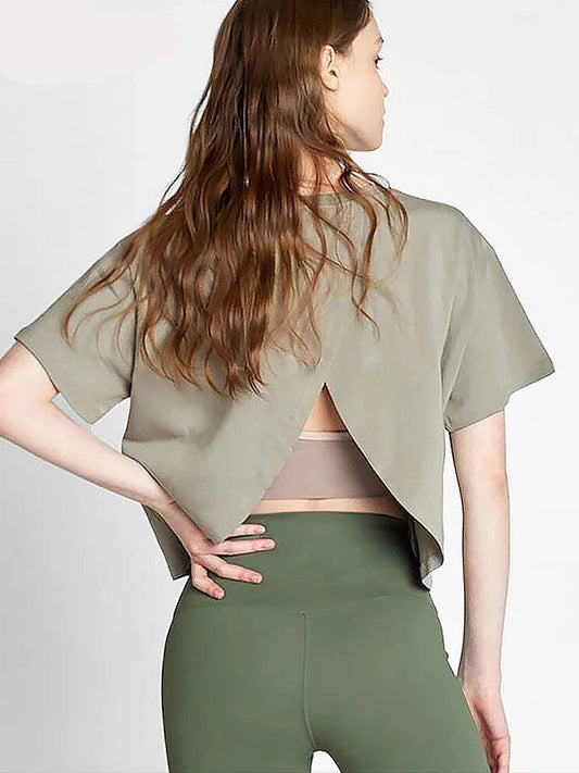 A woman wearing a green short-sleeve sports top with a back split design and matching green pants, standing with one hand on her back.