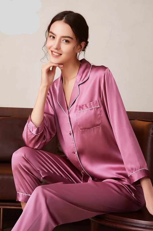 A woman sitting on a couch wearing a pink 100% Silk Pyjamas Set with long sleeves and a matching bottom, with a pocket on the front.