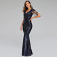A woman modeling a floor-length navy blue sequined gown with sheer sleeve details, posed against a solid light gray studio background.