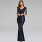 A woman modeling a floor-length navy blue sequined gown with sheer cap sleeves and a V-neckline, photographed against a light gray studio background.