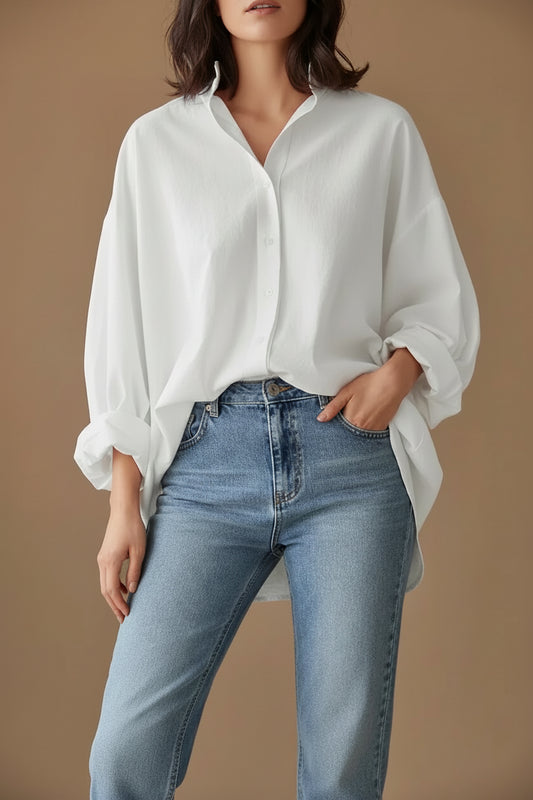 A woman wearing a white, long-sleeved, button-up blouse with an irregular hemline paired with blue jeans.