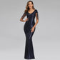 A woman modeling a floor-length navy blue sequined gown with sheer lace short sleeves and a V-neckline, photographed against a light gray studio background.