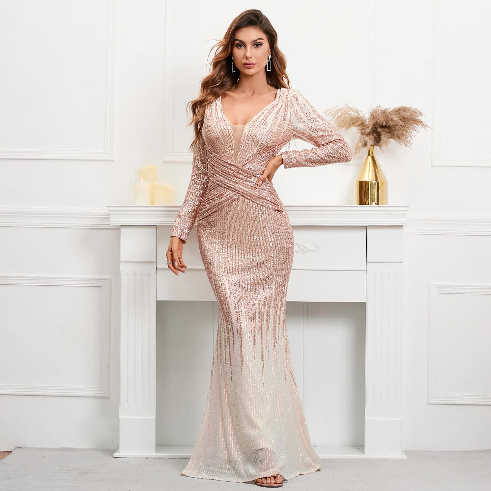 A woman models a long-sleeve, deep V-neck mermaid gown covered in shimmering rose gold sequins, standing in front of a white fireplace mantel.