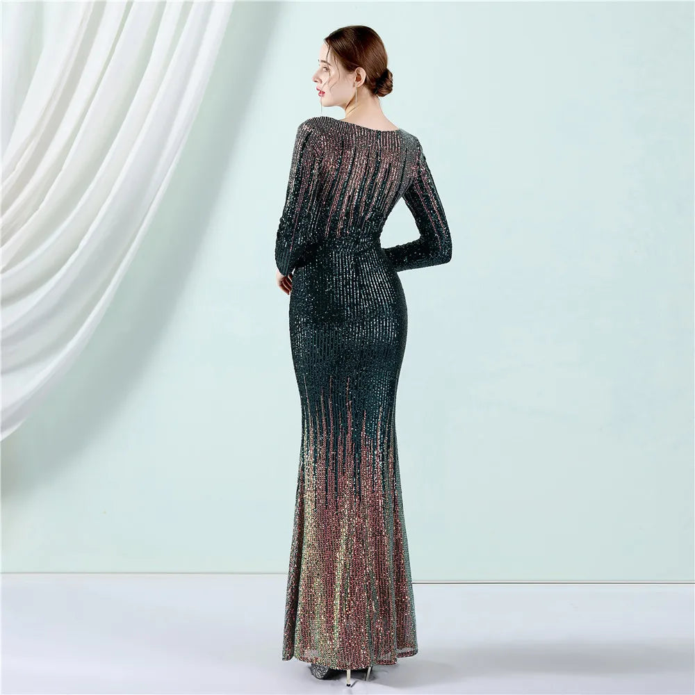 A woman stands with her back to the camera wearing a floor-length, long-sleeve mermaid gown covered in shimmering sequins that transition from dark teal at the top to bronze and rose-gold at the bottom, set against a pale mint studio backdrop with draped white fabric on the left.