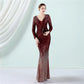 A woman modeling a long-sleeve, deep V-neck, floor-length mermaid gown covered in shimmering sequins. The dress features a dark burgundy red bodice that transitions into a sparkling rose gold gradient toward the flared hem.