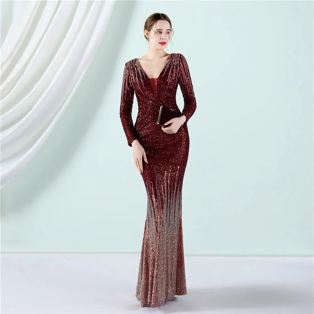A woman modeling a long-sleeve, deep V-neck, floor-length mermaid gown covered in shimmering sequins. The dress features a dark burgundy red bodice that transitions into a sparkling rose gold gradient toward the flared hem.