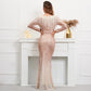 A woman stands with her back to the camera wearing a long-sleeve, floor-length sequined gown in a pale blush pink or champagne tone. The dress has a fitted silhouette with a mermaid-style flared hem and a sheer mesh overlay.