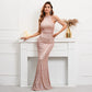 A woman models a rose gold sequined mermaid gown with sheer shoulder straps, posing in front of a white fireplace mantel.